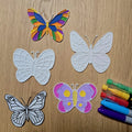 Colorful and white butterfly cutouts with markers on a wooden surface