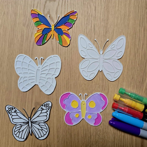 Colorful and white butterfly cutouts with markers on a wooden surface