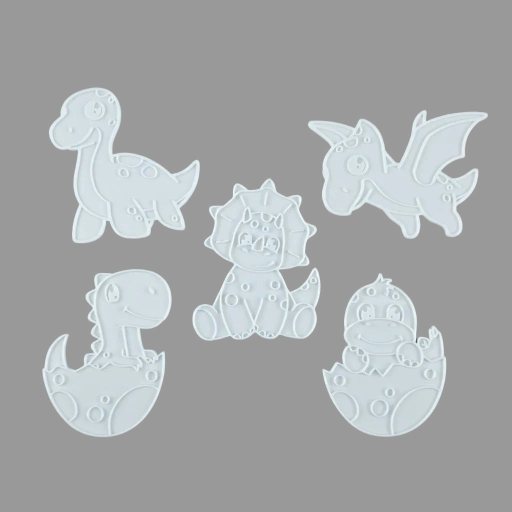 Five white plastic dinosaur-shaped cookie cutters or molds arranged on a light gray background, including a long-necked dinosaur, a flying dragon, a seated triceratops, a baby dinosaur hatching from an egg, and another hatching dinosaur.