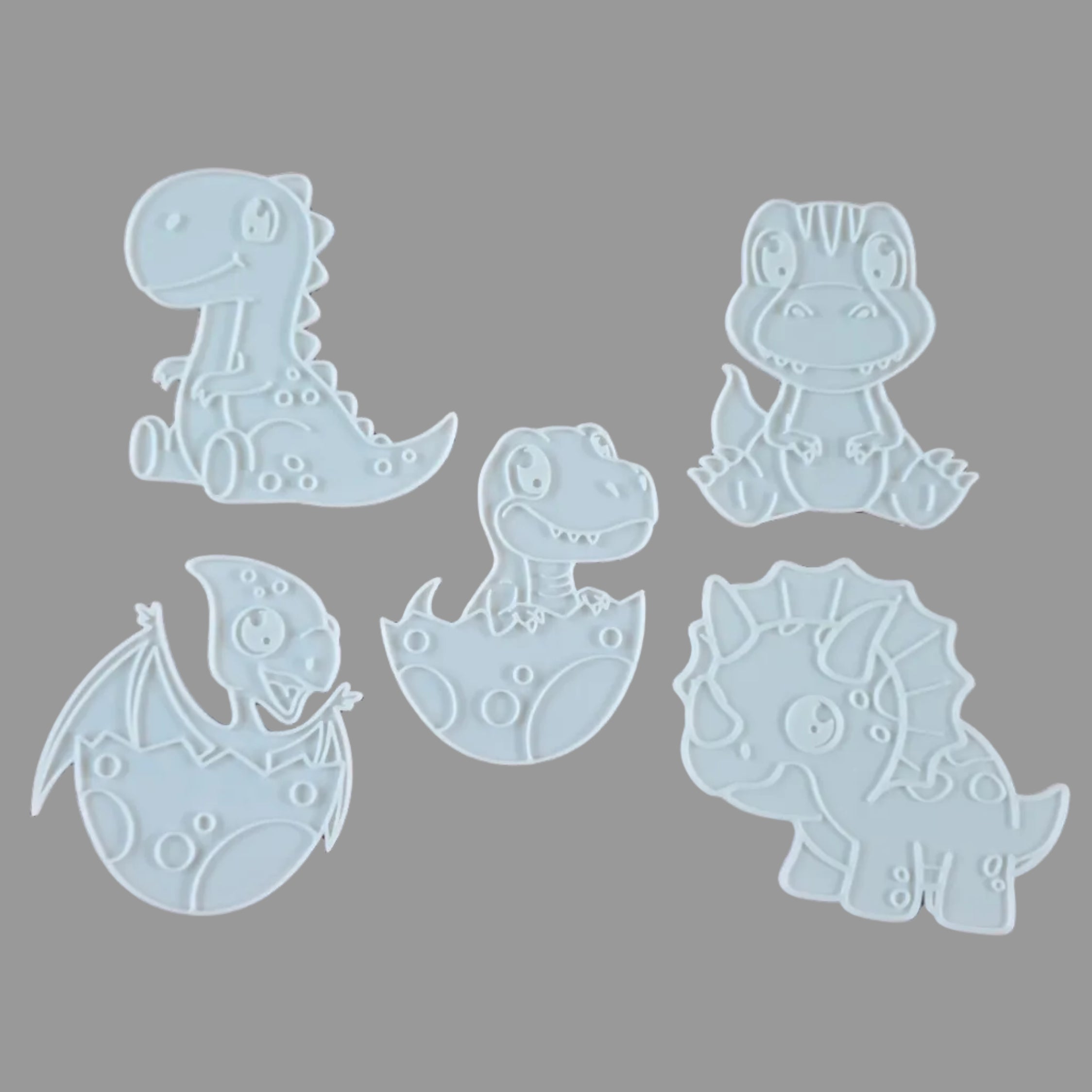 Five white dinosaur-shaped cookie cutters or stencils arranged on a grey background.