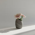 Gray textured vase with a pink flower on a light gray background